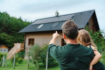 Vater mit Kind zeigt auf Haus mit Photovoltaikanlage
