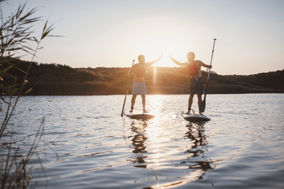 Zwei Personen fahren SUP Board bei Sonnenuntergang am See
